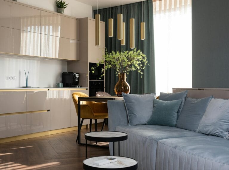 Kitchen interior with light cabinets at table with flowers in vase placed near soft sofa in modern apartment with window